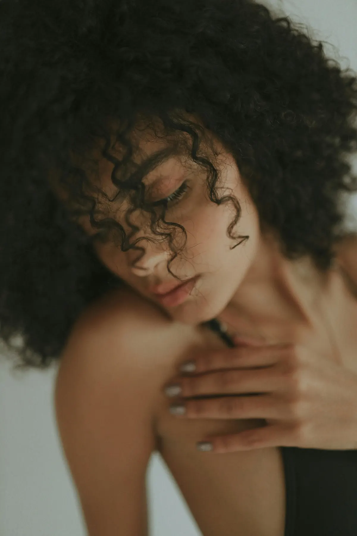 Soft-focus portrait of a woman with curly hair, hand resting on her chest